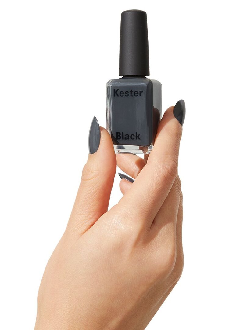 Eine Frauenhand hält einen grauen Nagellack hoch