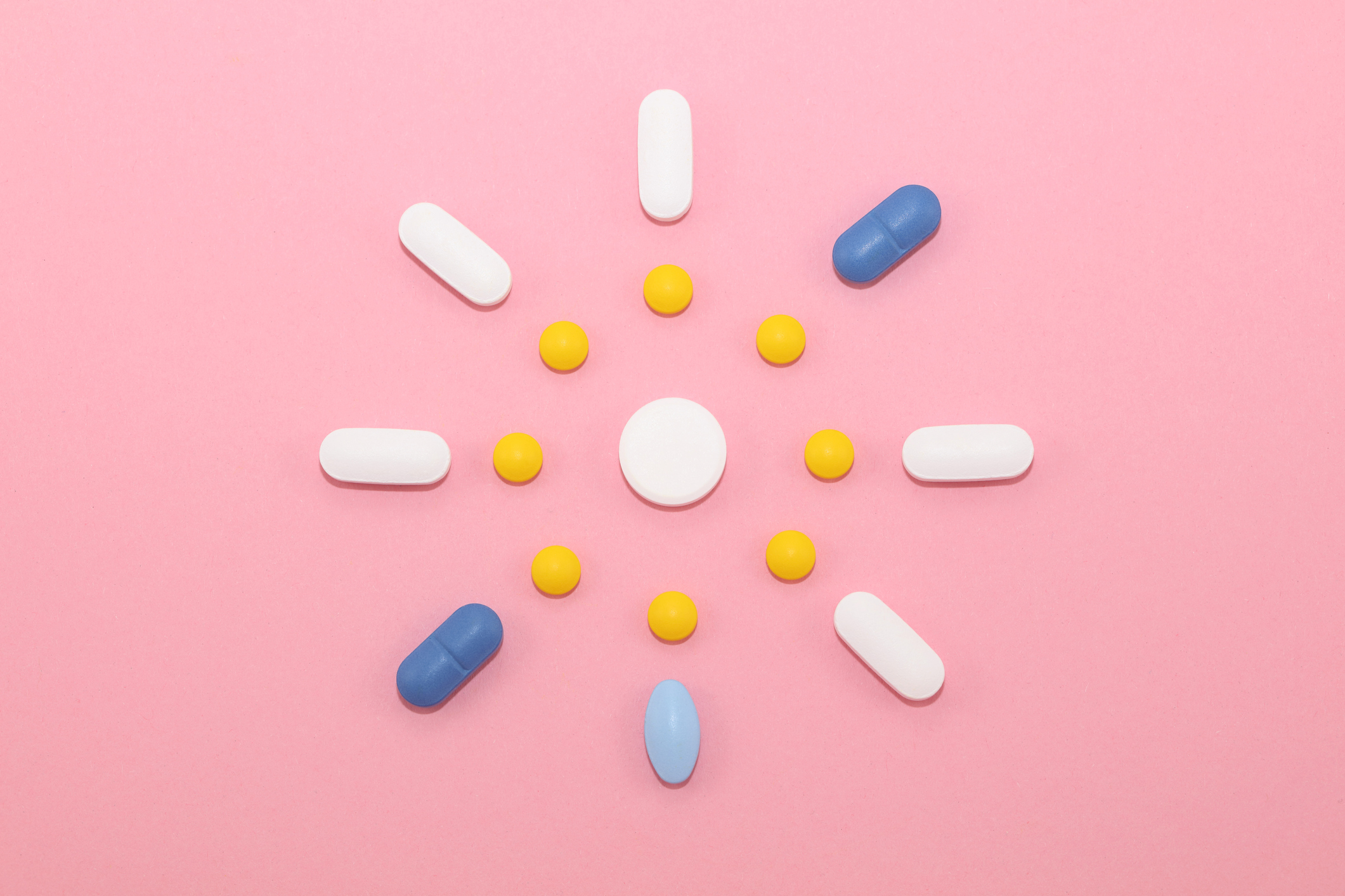 Tabletten und Kapseln wie eine Sonne auf rosa Untergrund arrangiert