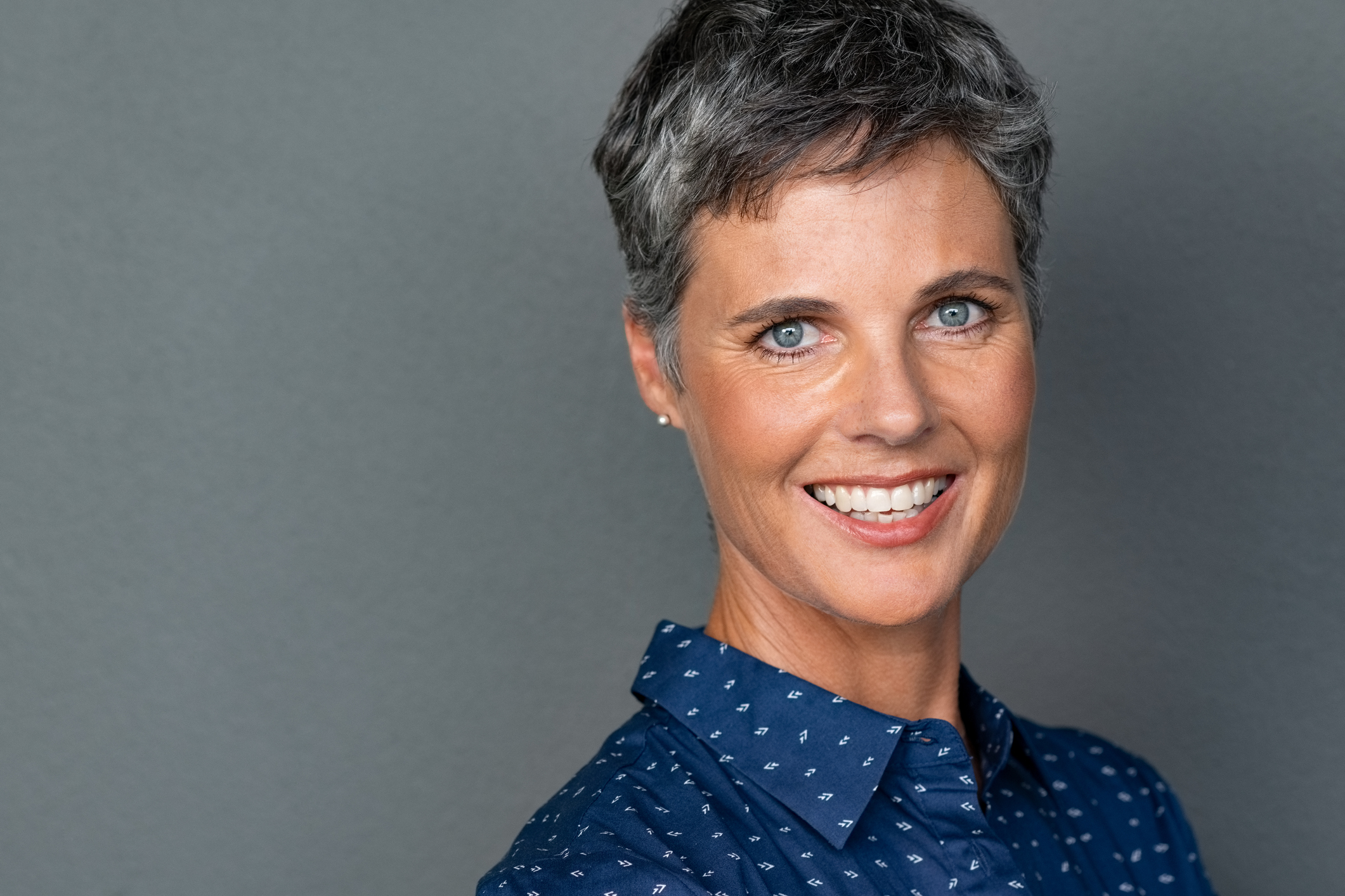 Strahlend lächelnde Frau mit lauen Augen und kurzen grauen Haaren