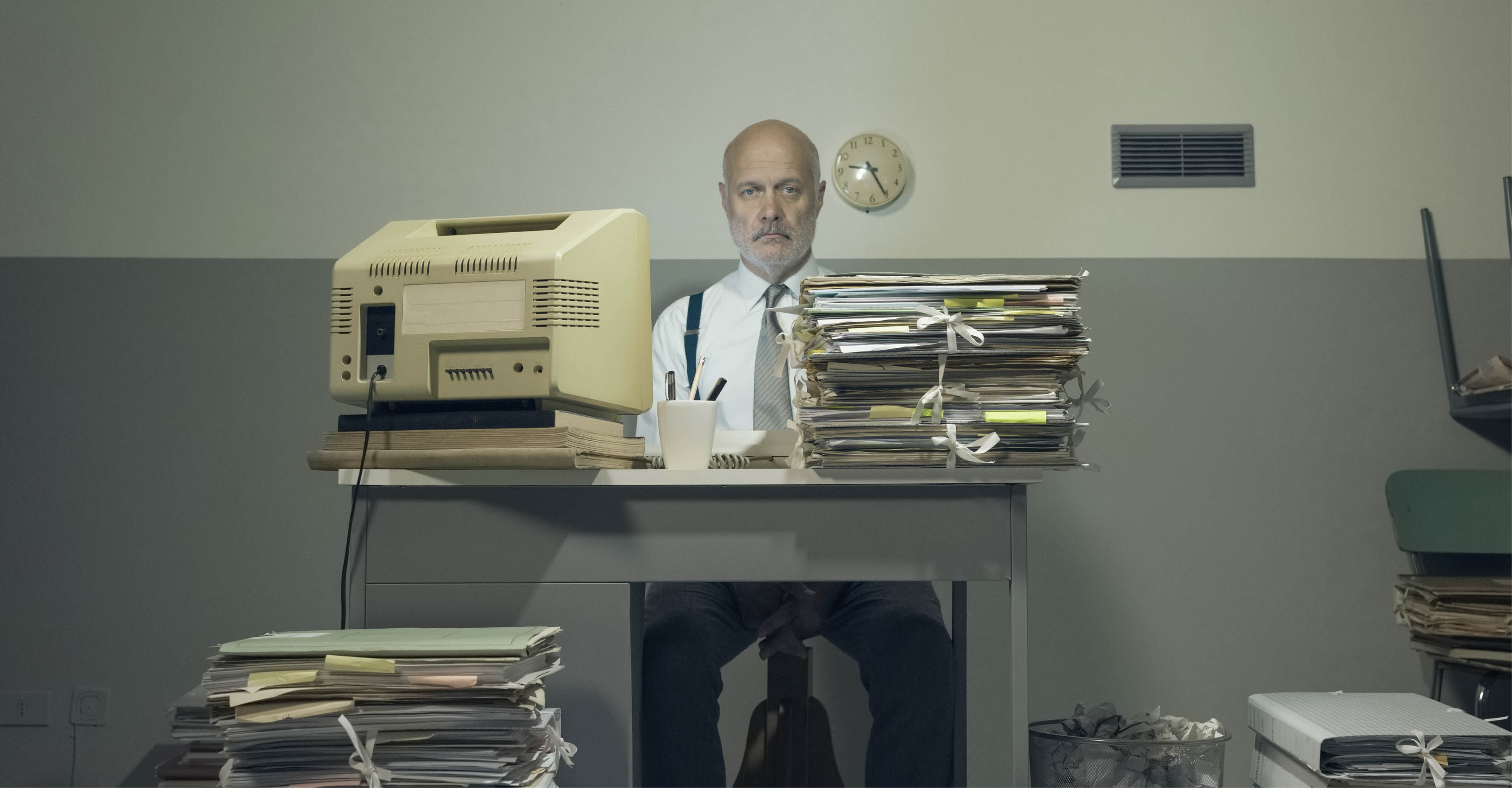 Beamter mit Aktenstapel in veraltetem Büro