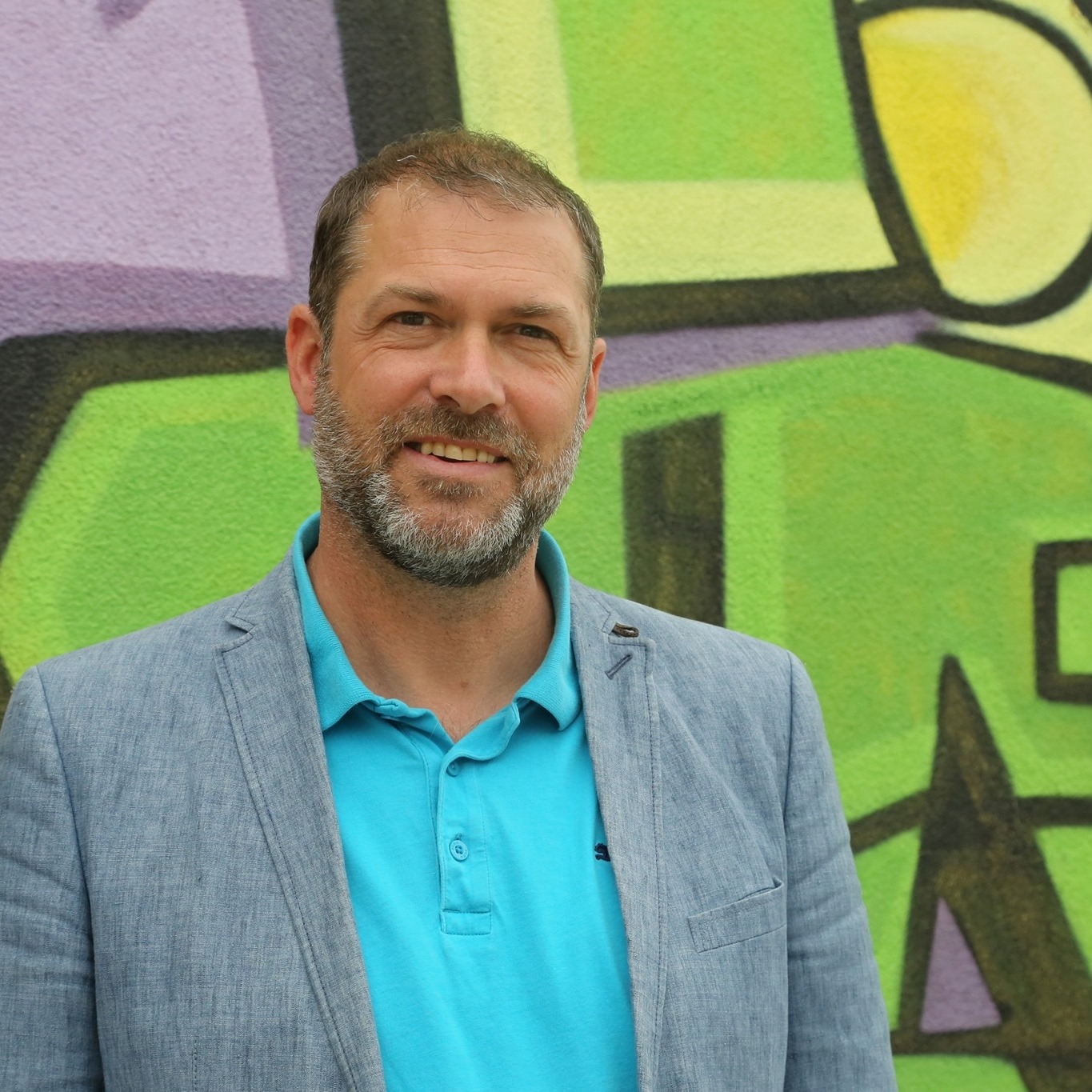 Stadtrat Markus Geiger steht vor einer mit Graffiti bemalten Wand.