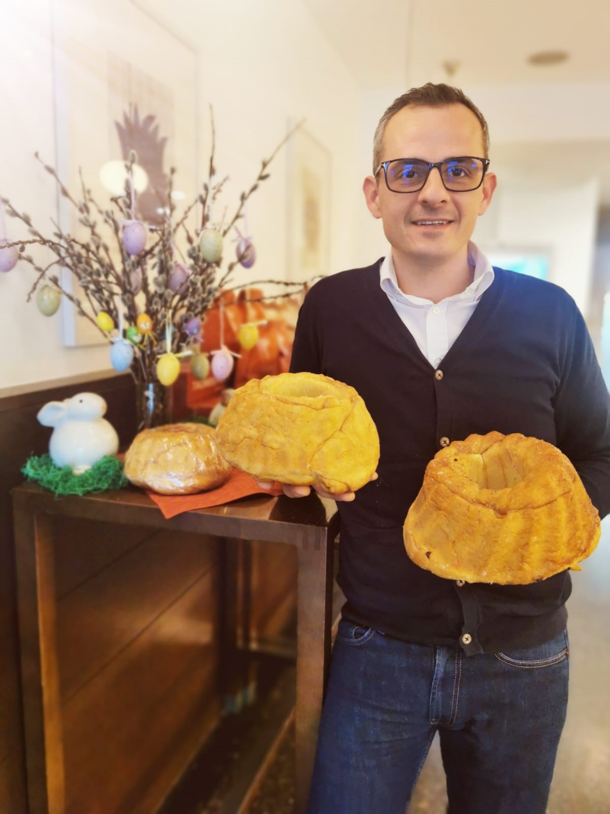 Bäckermeister Taumberger mit zwei Osterreindlingen in den Händen vor einem osterlich dekorierten Tisch