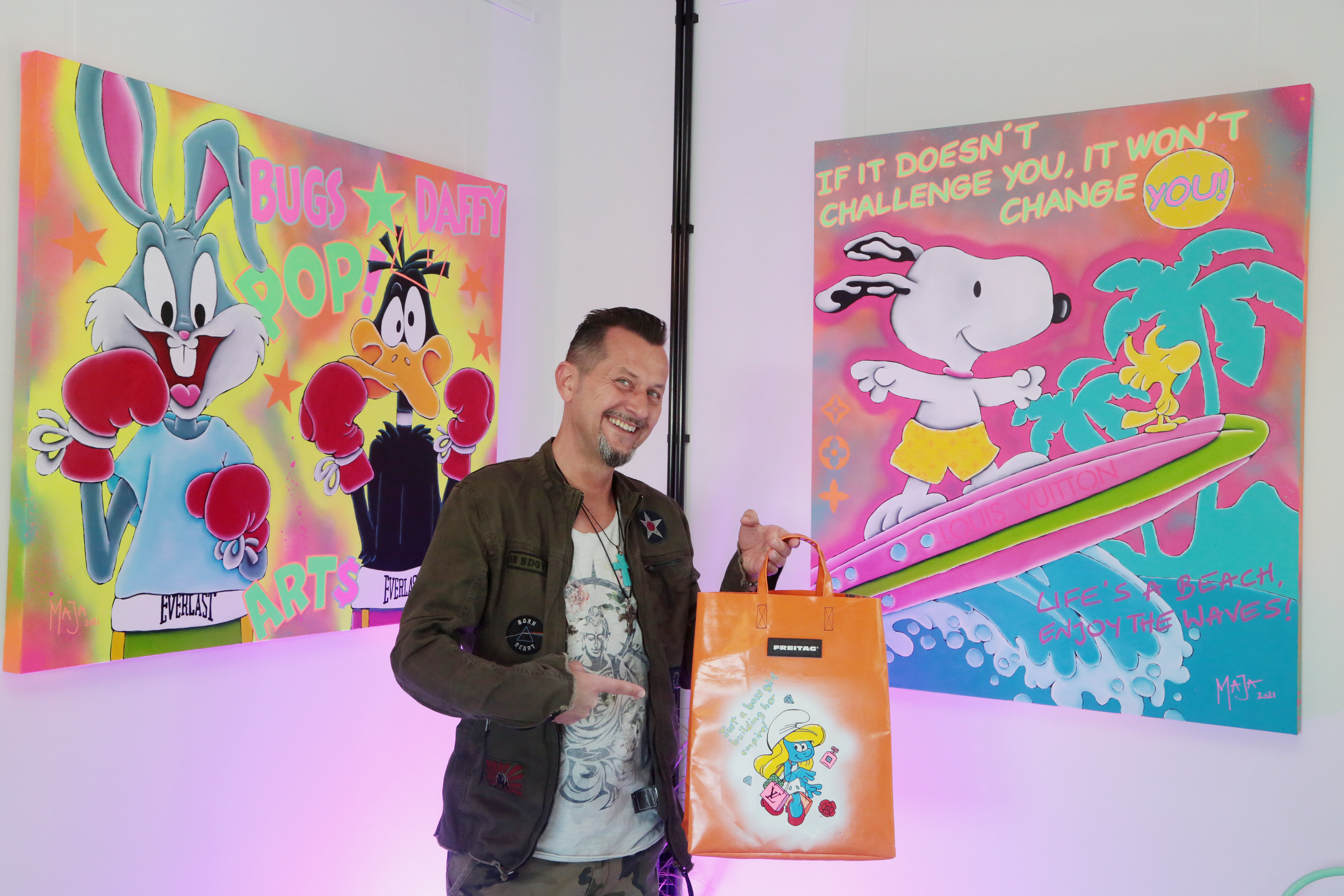 Pop-Art-Künstler Mario Stroitz vor zwei Bildern von Bugs Bunny und Daffy Duck in Boxausrüstung sowie Snoopy beim Sürfen