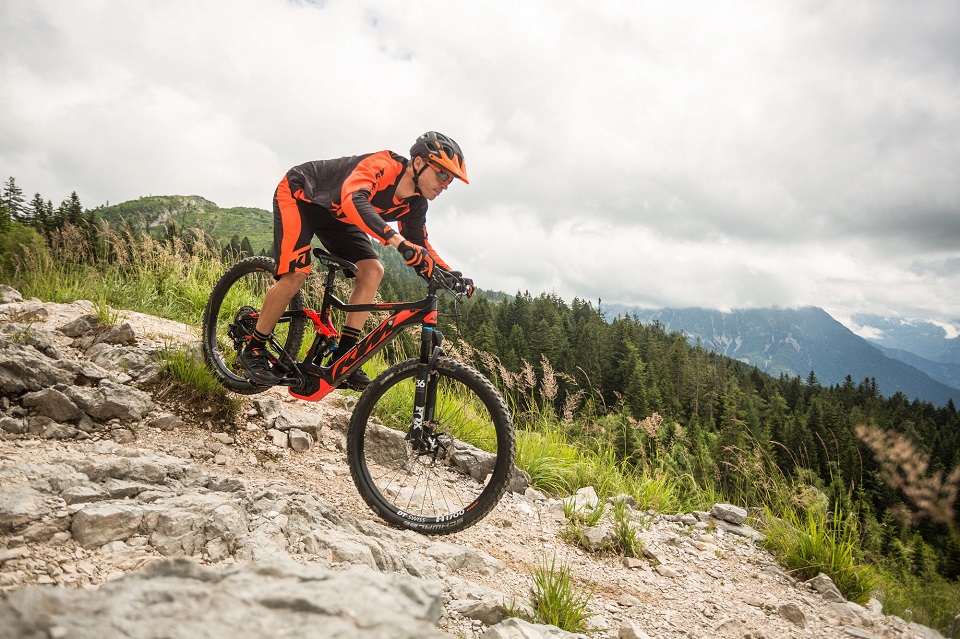 Mann mit Helm und Fahrradtrikot fährt mit einem E-Bike von KTM einen felsigen Berg hinunter.
