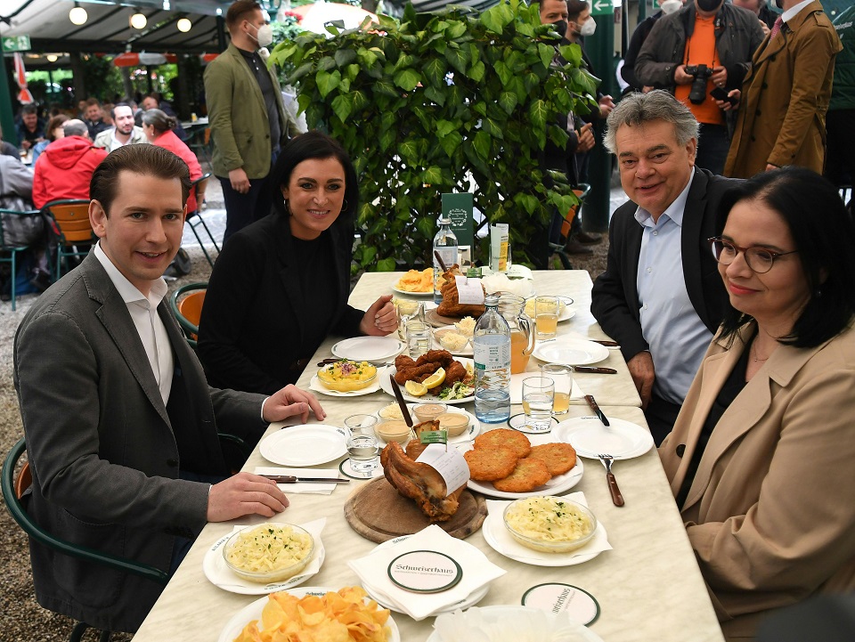 (v.l.) Bundeskanzler Sebastian Kurz (ÖVP), Landwirtschaftsministerin Elisabeth Köstinger (ÖVP), Vizekanzler Werner Kogler (Grüne) und Staatssekretärin Andrea Mayer (Grüne) sizen im Schweizerhaus an einem Tisch mit Stelze, Beilagen und Mineralwasser.