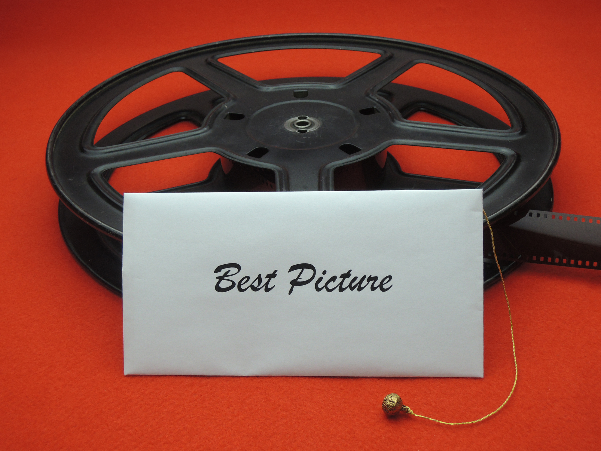 Eine schwarze Filmrolle auf einem roten Teppich an die ein weißer Briefumschlag mit der Beschriftung Best Picture angelehnt ist