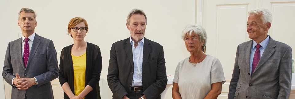 Fünf Menschen stehen nebeneinander, sie posieren für ein Foto. Die Aufnahme zeigt sie von der Hüfte aufwärts. Sie tragen förmliche Kleidung.