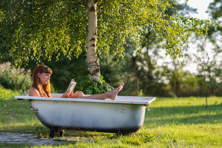 Frau sitzt in einer Badewanne im sommerlichen Garten