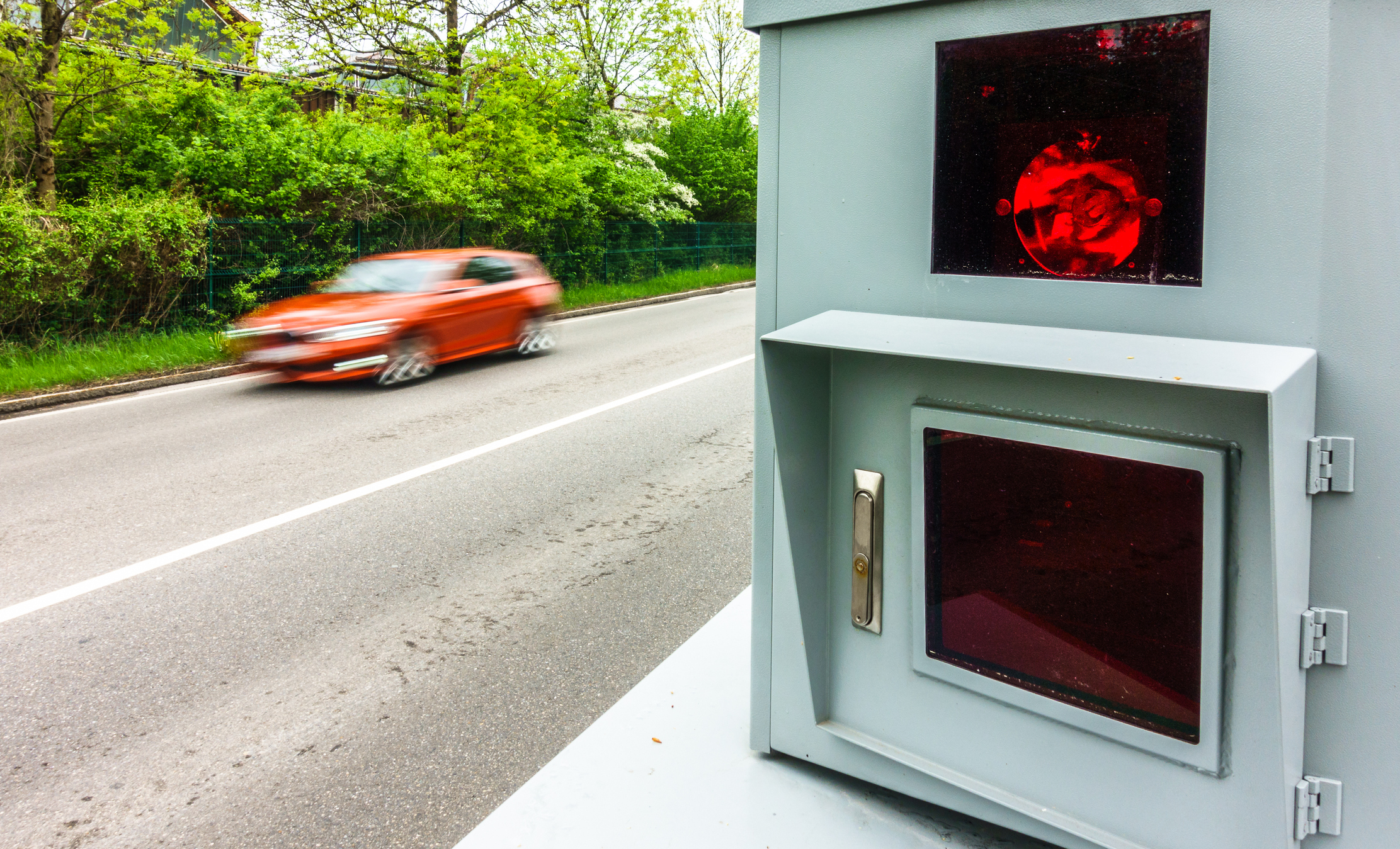 Ein oranges Auto fährt in hohem Tempo an einer Radarfalle vorbei