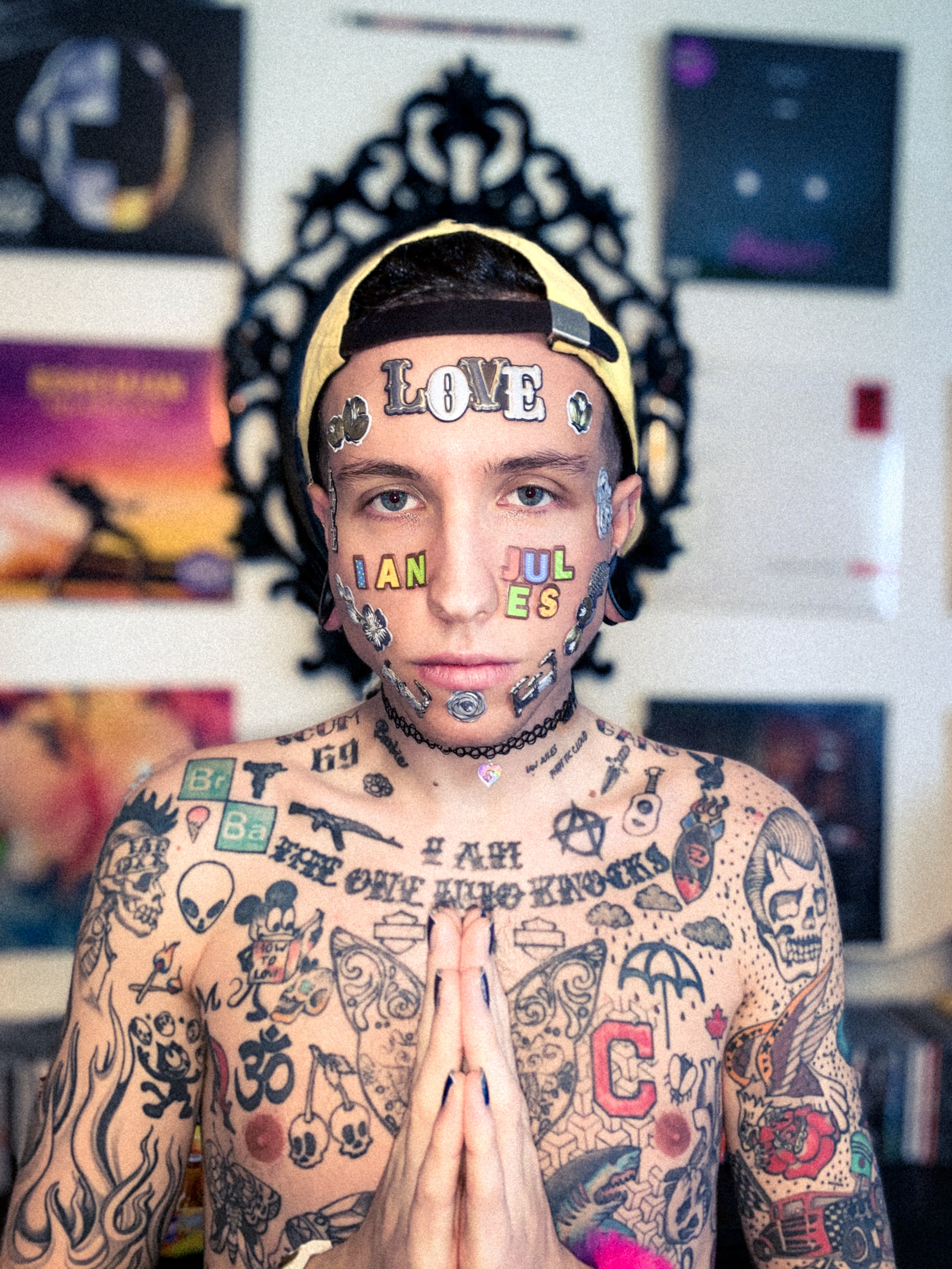 Ian Jules mit gefalteten Händen und stark tätowiertem nacktem Oberkörper vor einer Wand mit Schallplatten