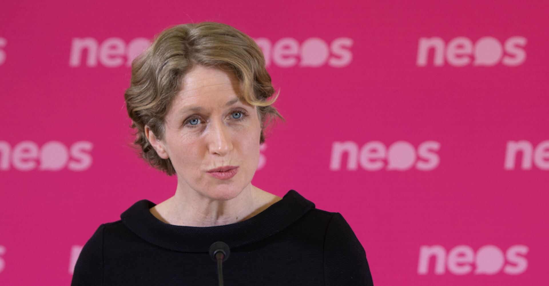 NEOS Mandatarin Stephanie Krisper im Porträt vor einem pinken Neos-Hintergrund | Credit: Alex Halada / picturedesk.com