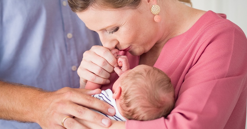 Eine glückliche Ministerin Susanne Raab hält ihr Baby im Arm und küsst seine Hand. Ihr Mann hat die Hand auf ihren Arm gelegt.