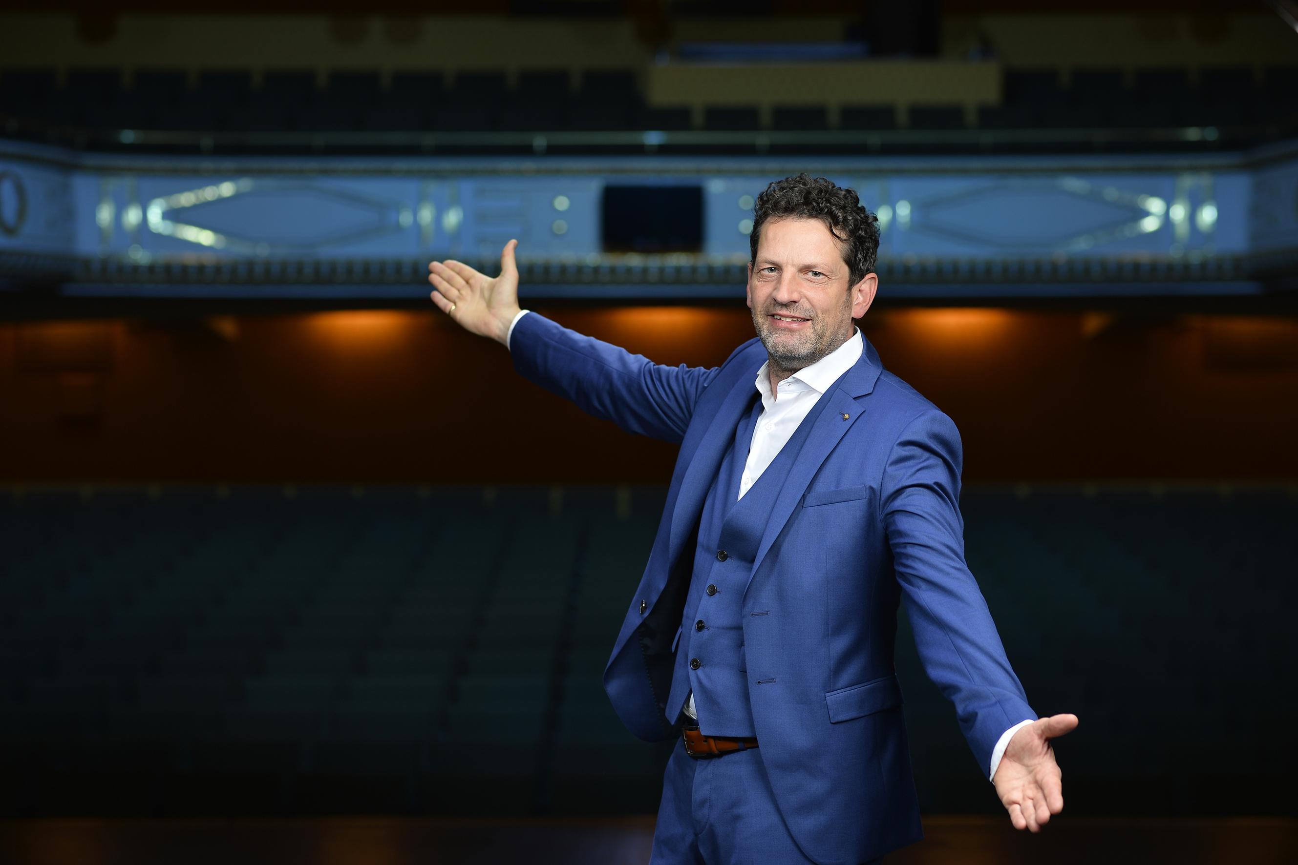 Stadttheater-Intendant Aron Stiehl mit weit geöffneten Armen vor seiner Theaterkulisse