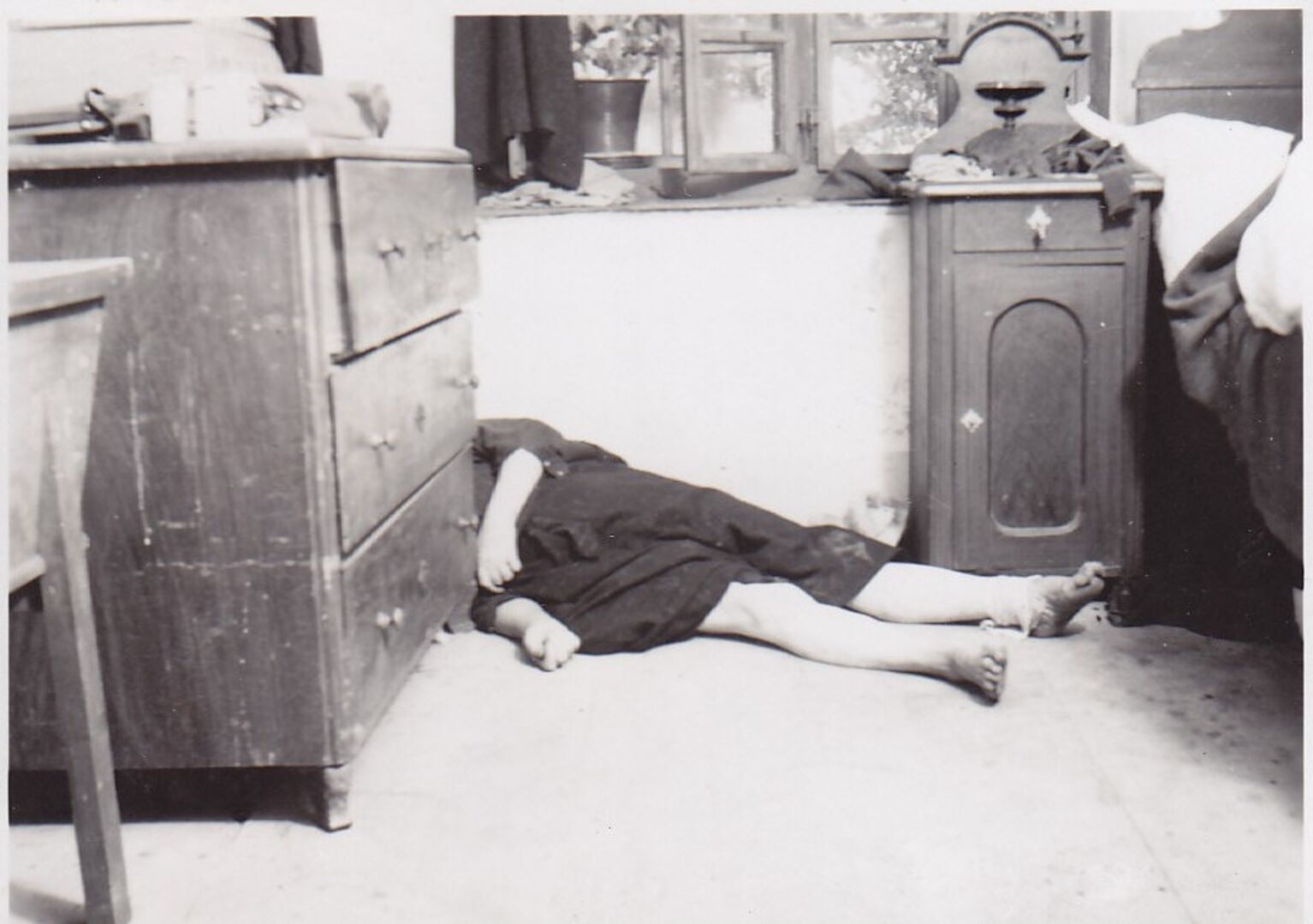 Der leblose, auf dem Boden eines Schlafzimmers liegende Körper einer Frau - ihr Kopf wird von einer Kommode verdeckt