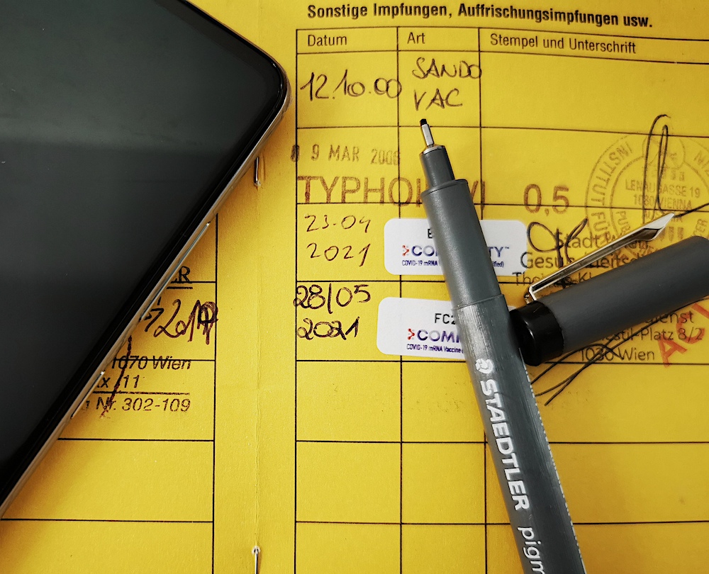 Ein aufgeblätterter Impfpass mit Enträgen, ein Stift verdeckt die Einträge