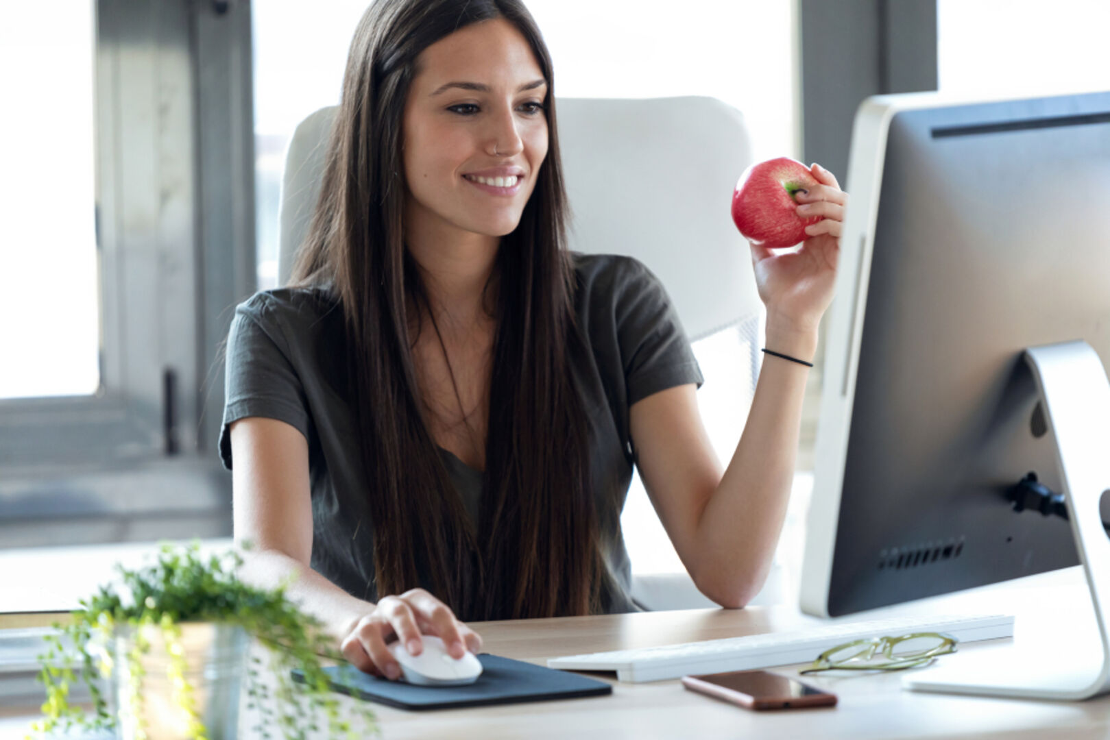Frau mit Apfel in der Hand vor dem Computer | Credit: iStock.com/nensuria