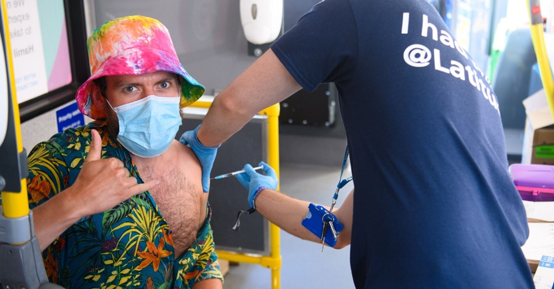 Ein Mann in einem bunten Batik-Shirt mit Maske wird in einem Festivalbus geimpft.