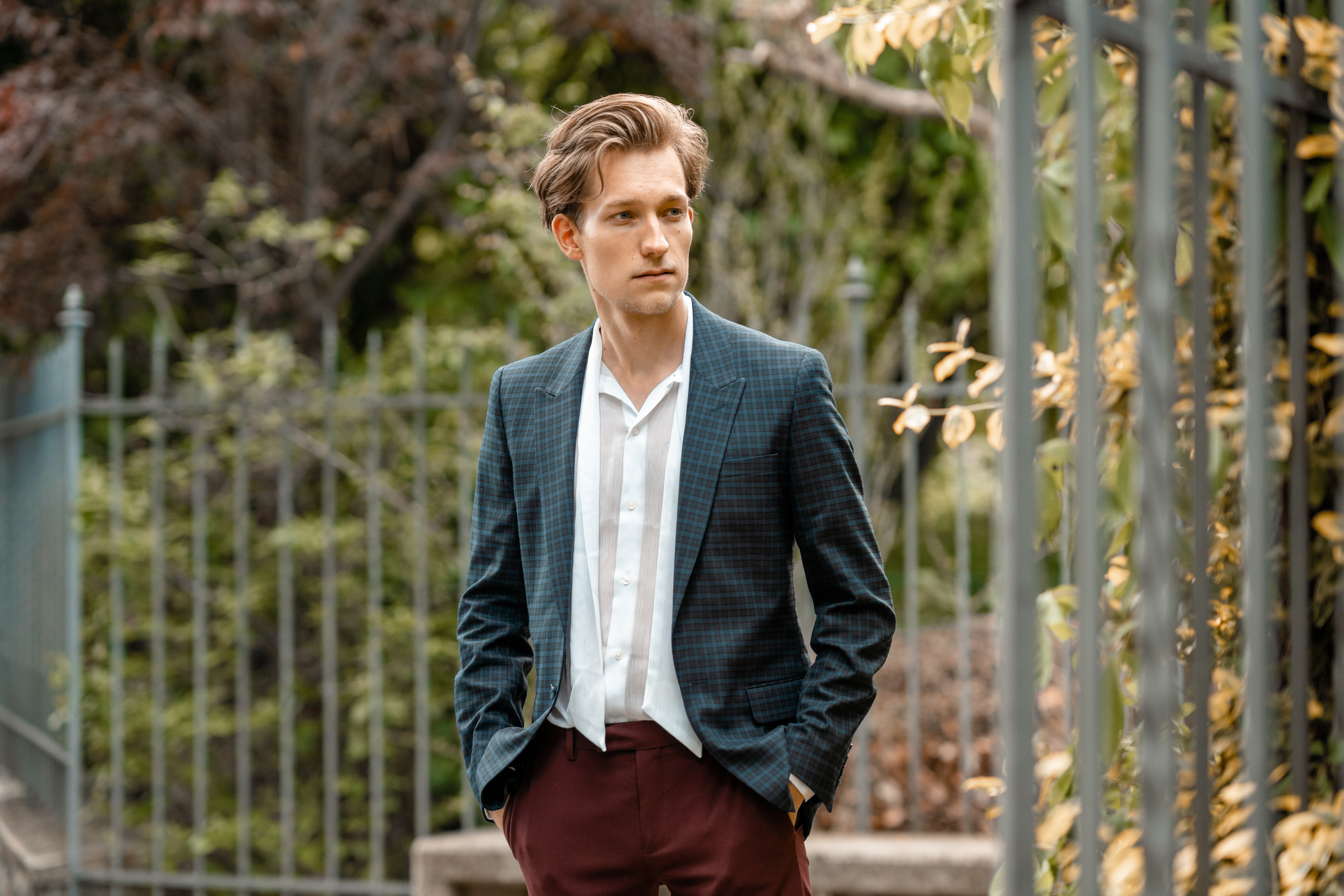 Der junge Musiker Simon Stadler steht, in einen modernen Anzug gekleidet, vor einem umzäunten Park
