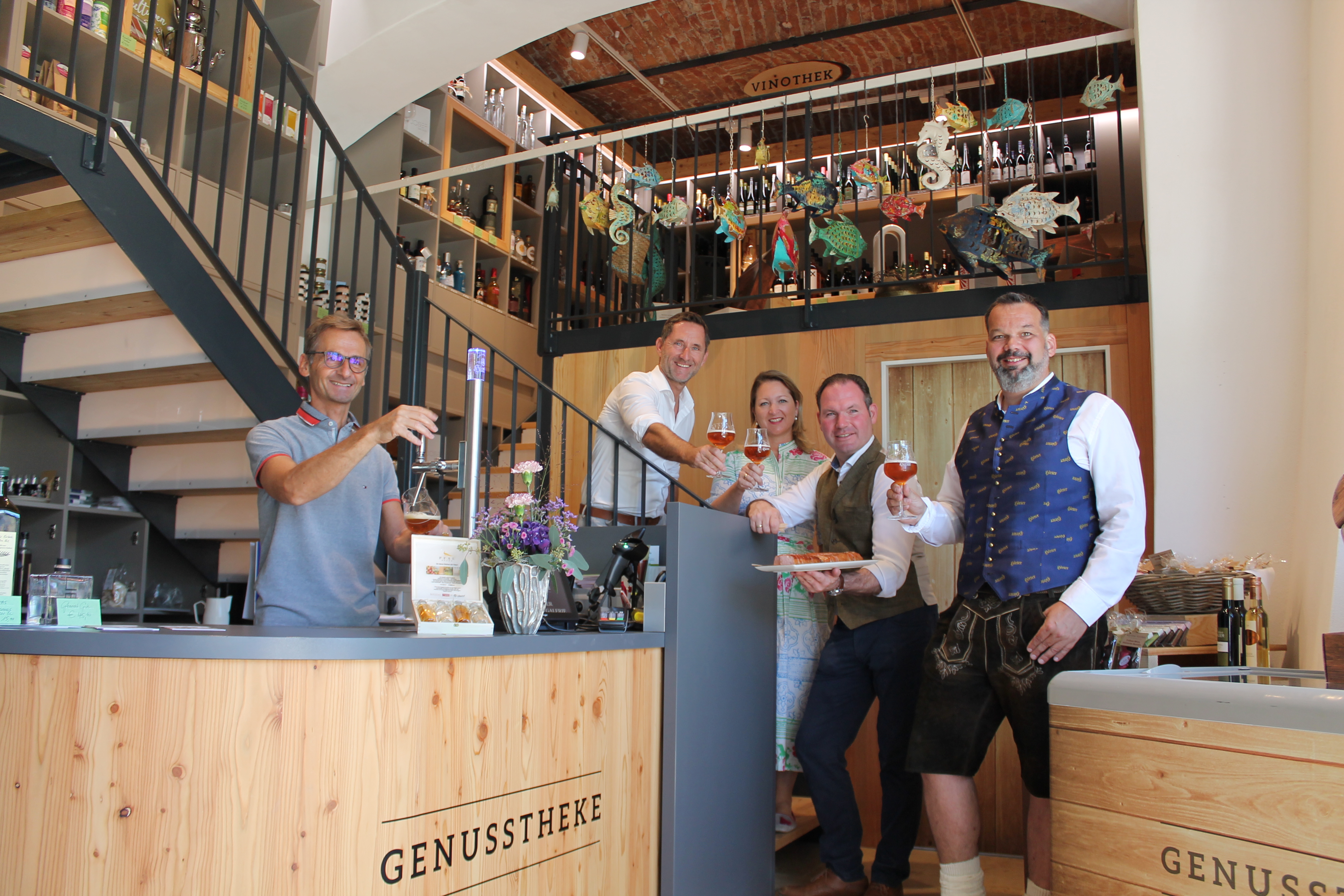 Vier Männer und eine Frau stehen vor einer Biertheke und prosten sich mit einem Glas Bier zu