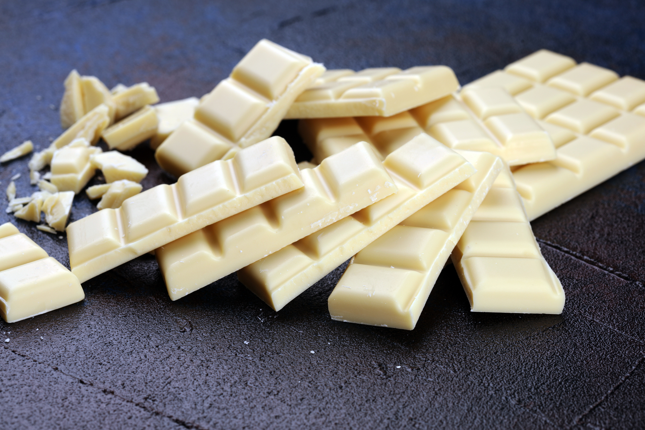 Mehrere Rippen weißer Schokolade auf einer dunklen Tischplatte