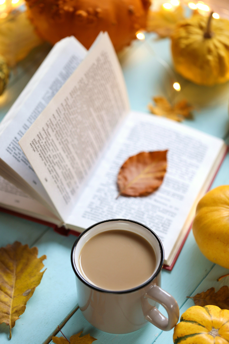 Teestunde mit aufgeschlagenem Buch, umrahmt von herbstlich verfärbten Blättern | Credit: iStock.com/ yul38885