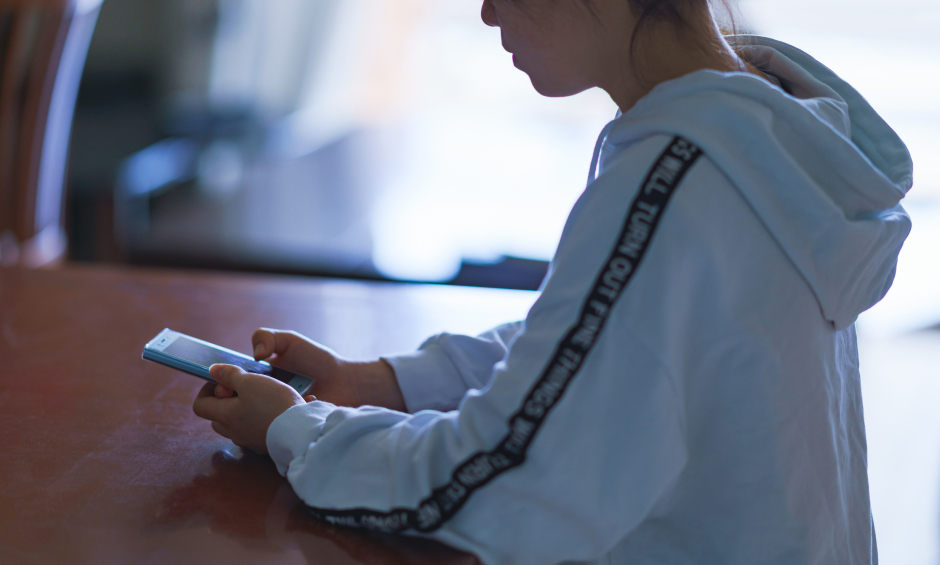 Asiatisches Mädchen sitzt über ihr Smartphone gebeugt | Credit: iStock.com/show999