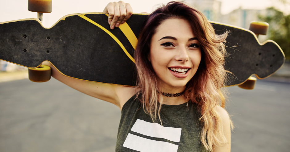 Junges Mädchen mit ihrem Skateboard hinter dem Körper verschränkt | Credit: iStock.com/diignat