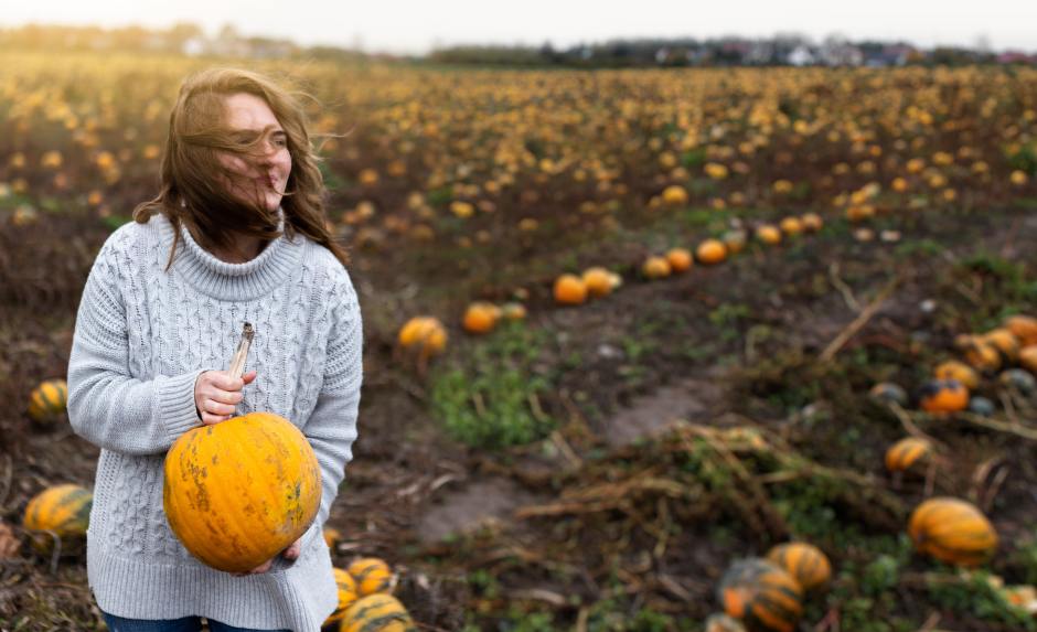 An einem düsteren, windigen Herbsttag hält eine Frau im Feld einen frisch geernteteten Kürbis in ihren Händen | Credit: iStock.com/Scharfsinn86