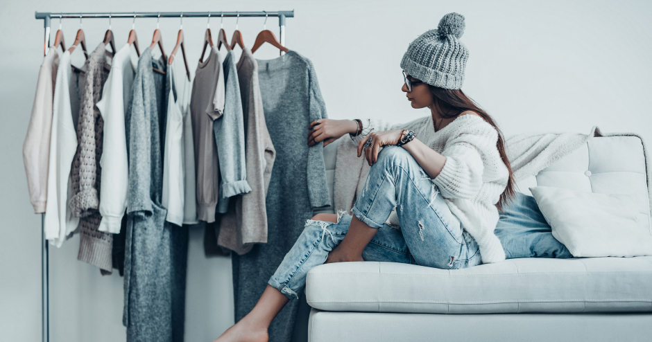 Junge Frau sitzt vor dem Kleiderständer und durchforstet ihre Garderobe | Credit: iStock.com/g-stockstudio