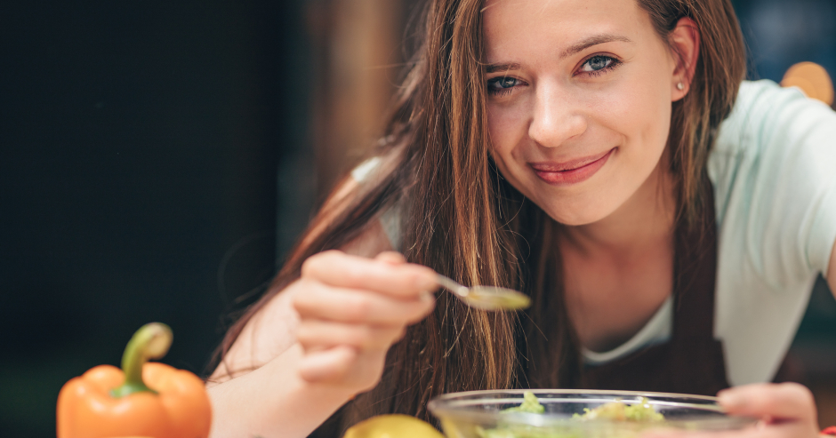 Eine junge Frau mit langen, braunen Haaren schmeckt zufrieden ihr Essen ab | Credit: iStock.com/Deklofenak