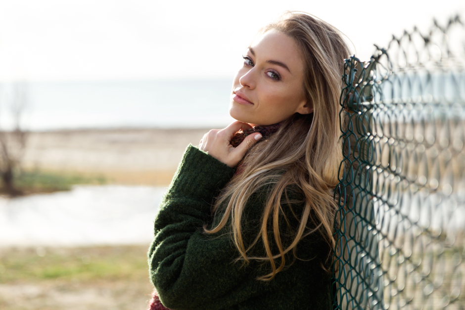 Junge, blonde Frau lehnt an einem sonnigen Wintertag an einem Zaun | Credit: iStock.com/nensuria