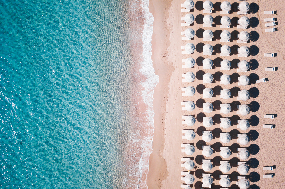 Luftaufnahme, die vier Reihen aufgespannter weißer Sonnenschirme an einem sardinischen Strandabschnitt zeigt | Credit: iStock.com/Travel Wild