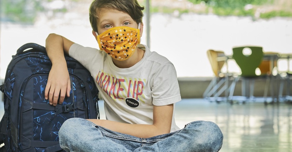 Ein etwa 10jähriger Schüler mit Stoffmaske sitzt in der Aula einer Schule