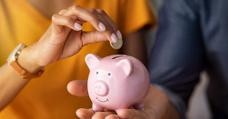 Paar hält gemeinsam ein Sparschwein, in das sie eine Münze einwirft | Credit: iStock.com/Ridofranz