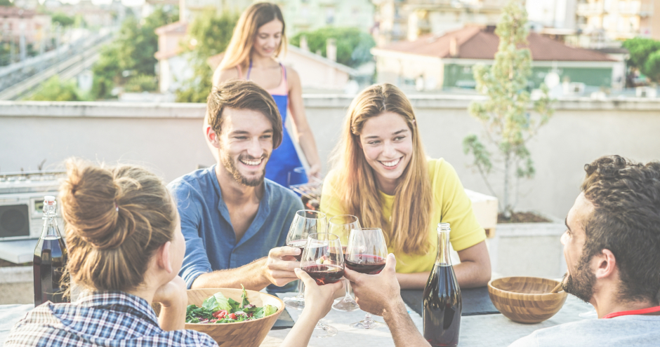 Junge Menschen genießen eine gemeinsame Mahlzeit unter freiem Himmel auf einer Dachterrasse | Credit: iStock.com/DisobeyArt