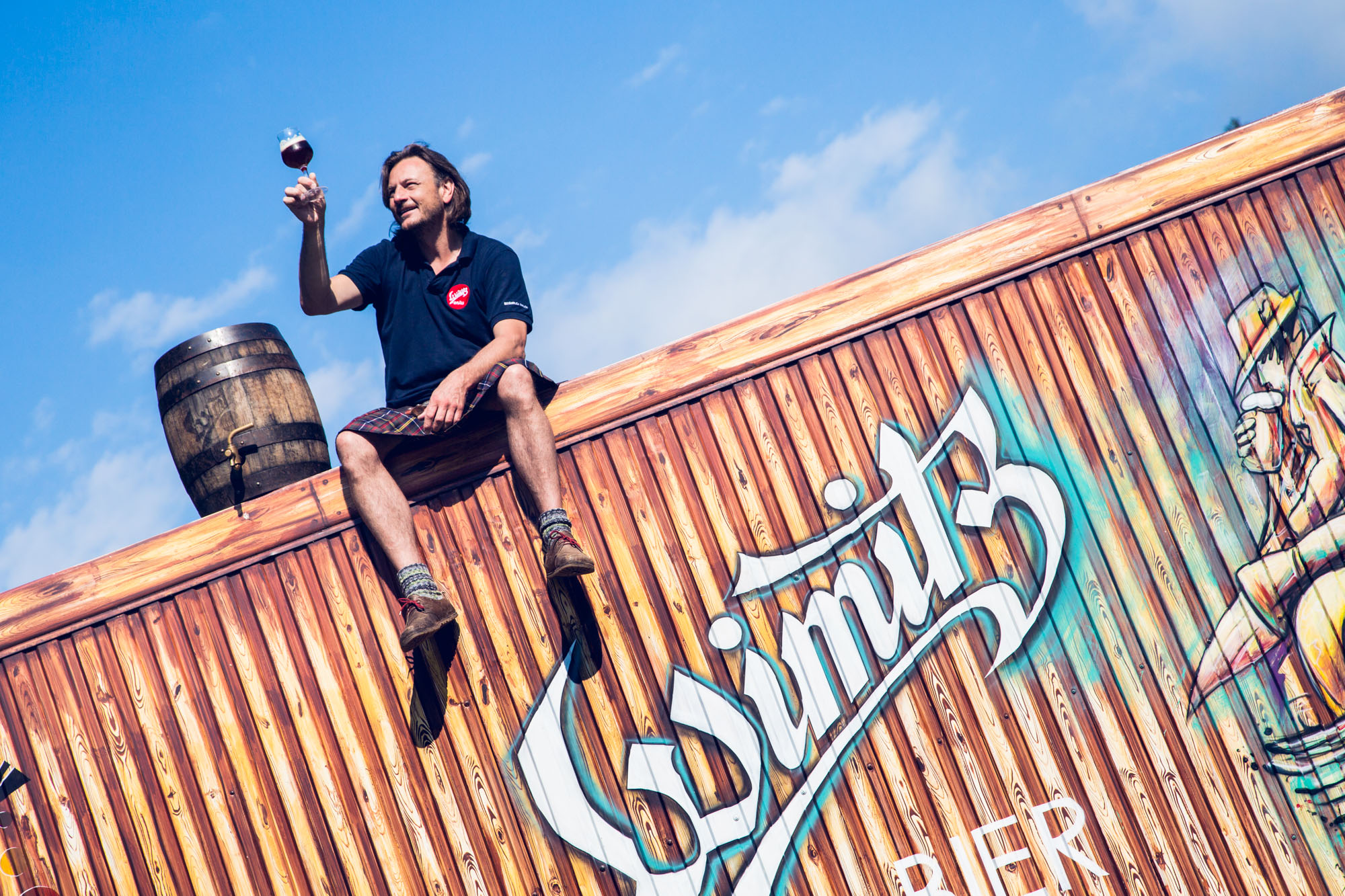 Josef Habich sitzt in einen Kärntner Kilt gekleidet auf dem Dach seiner Brauerei und hält ein Bierglas in die Höhe