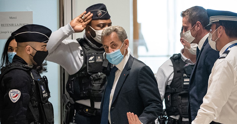 Nicolas Sarkozy mit Maske, umgeben von französischen Polizisten.