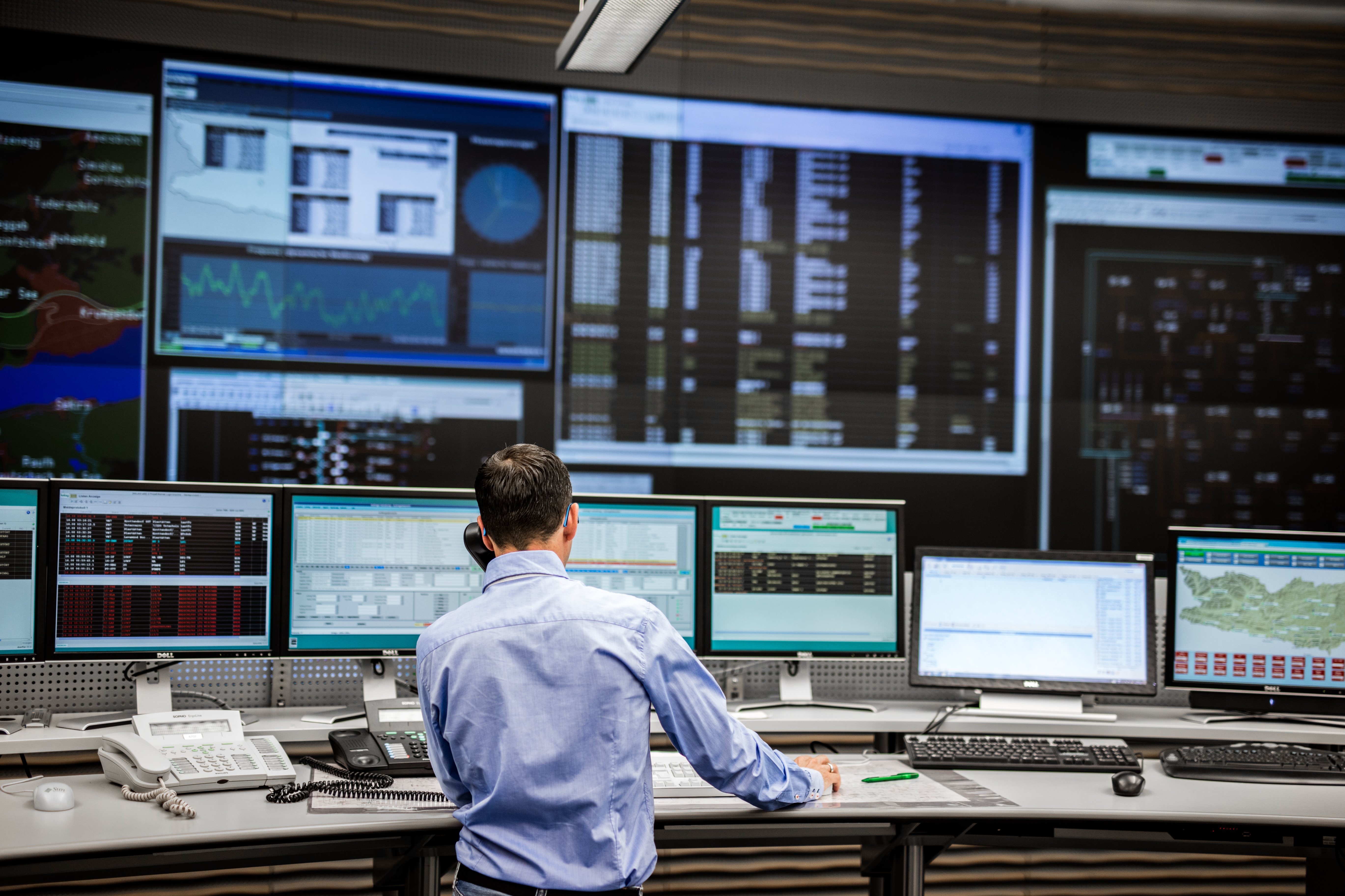 Ein Mann steht mit einem Telefonhörer am Ohr vor unzähligen Bildschirmen in der Schaltzentrale der Kärnten Netz GmbH