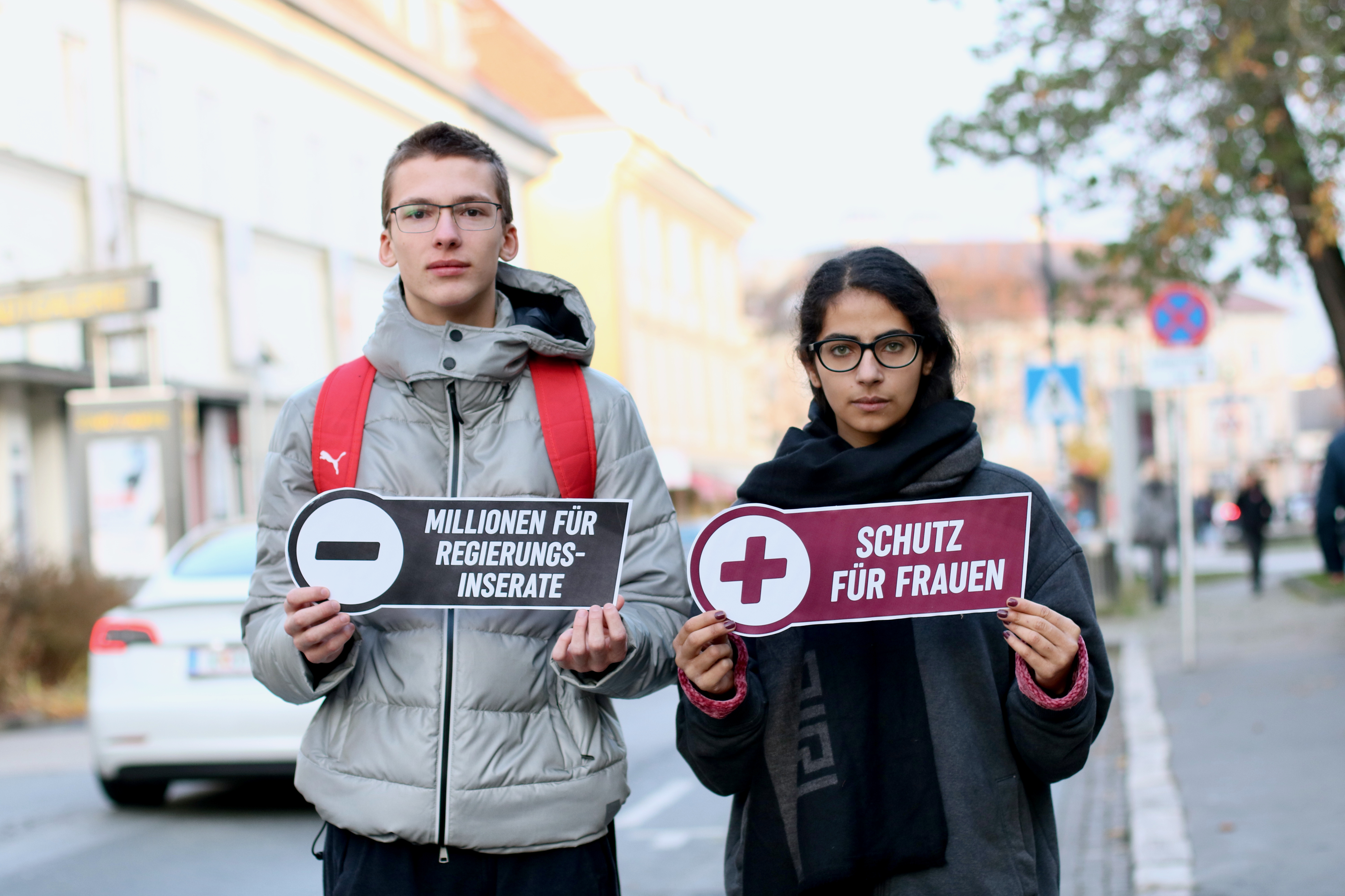 Ein junger Mann und eine junge Frau halten zwei Schilder mit Botschaften für mehr Gewaltschutz für Frauen in die Kamera