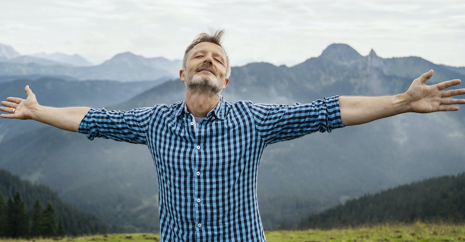 Mann breitet Arme aus und schließt die Augen vor Bergkulisse