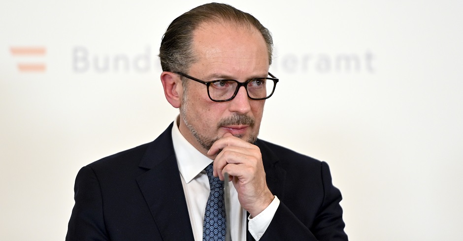 Bundeskanzler Alexander Schallenberg im Halbporträt vor der Pressewand des Bundeskanzleramts. Er hat die Hand an das Kinn gelegt und wirkt nachdenklich.