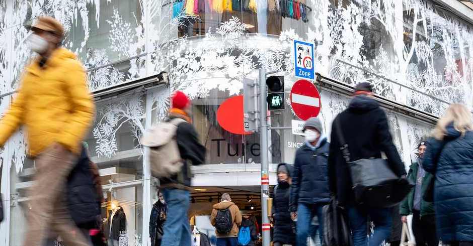 Menschen mit FFP2-Maske und Winterkleidung eilen an Geschäften vorbei