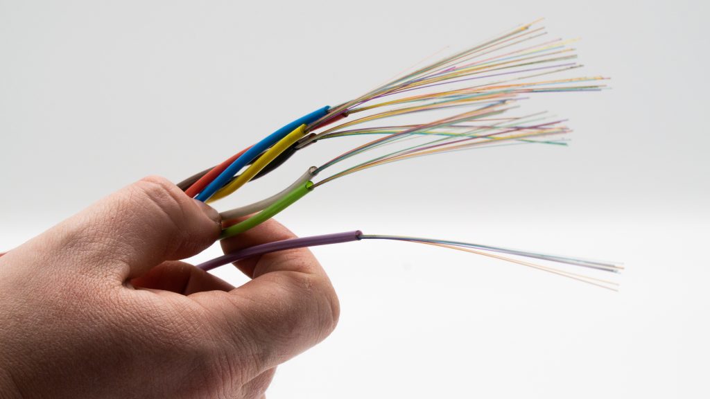 Eine männliche Hand hält bunte Kabel mit Glasfaser