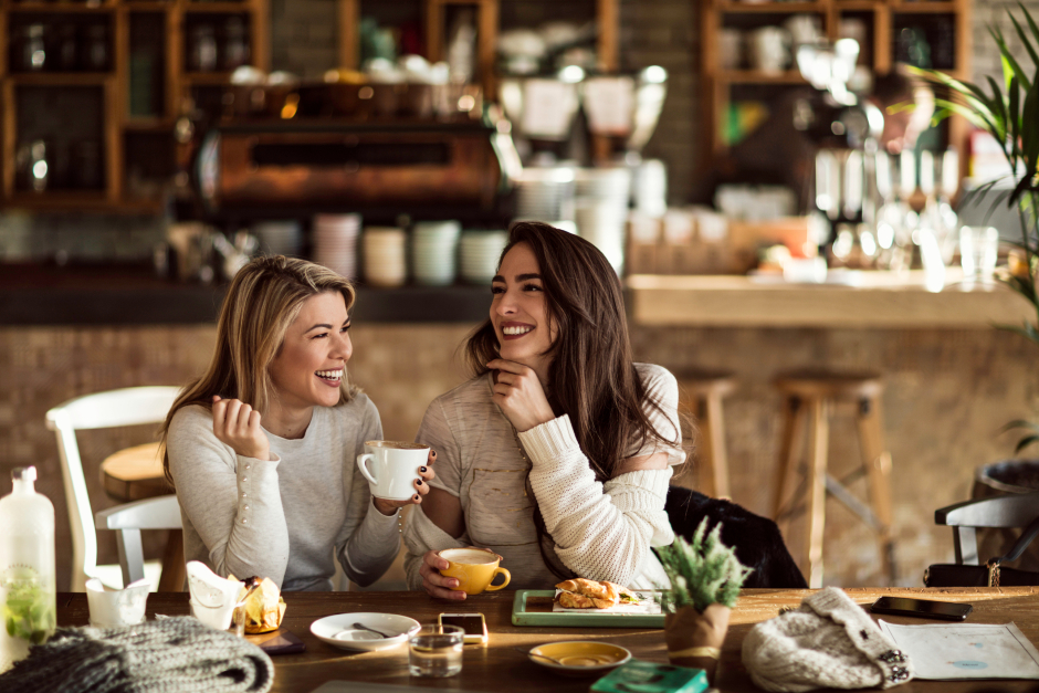 Zwei Frauen lachen beim gemeinsamen Kaffeeplausch in einem Café | Credit: iStock.com/Drazen Zigic