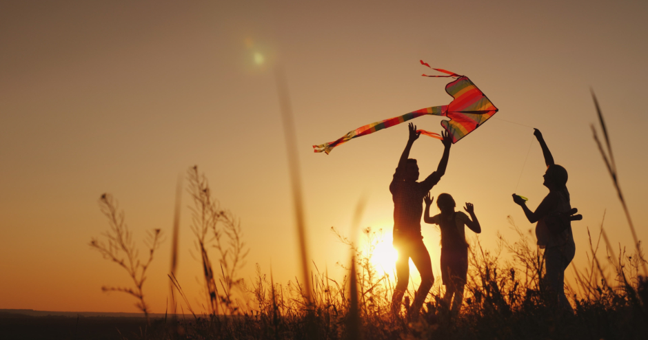 Im Sonnenuntergang lässt eine dreiköpfige Familie einen Drachen steigen | Credit: iStock.com/StockSeller_ukr