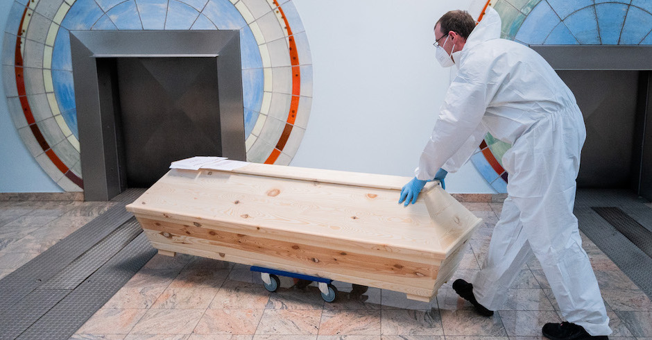 Mann in Schutzanzug schiebt Sarg Richtung Öffnung des Ofens