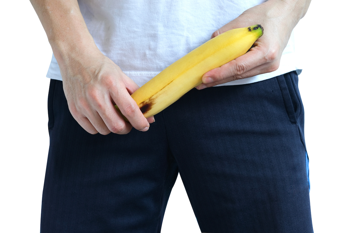 Ein Mann in Jeans hält sich eine nach oben weisende  Banane vor den Schritt