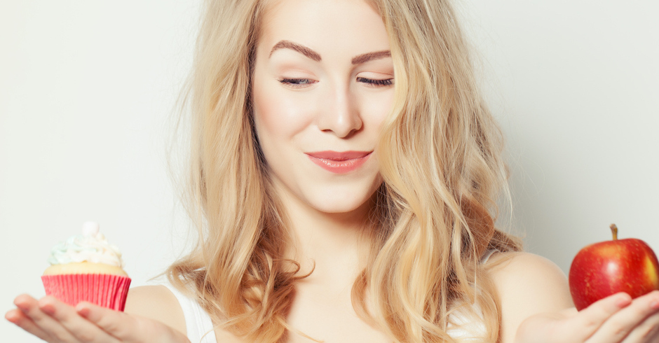 Junge blonde Frau hält in der einen Hand Cupcake, in der anderen Apfel