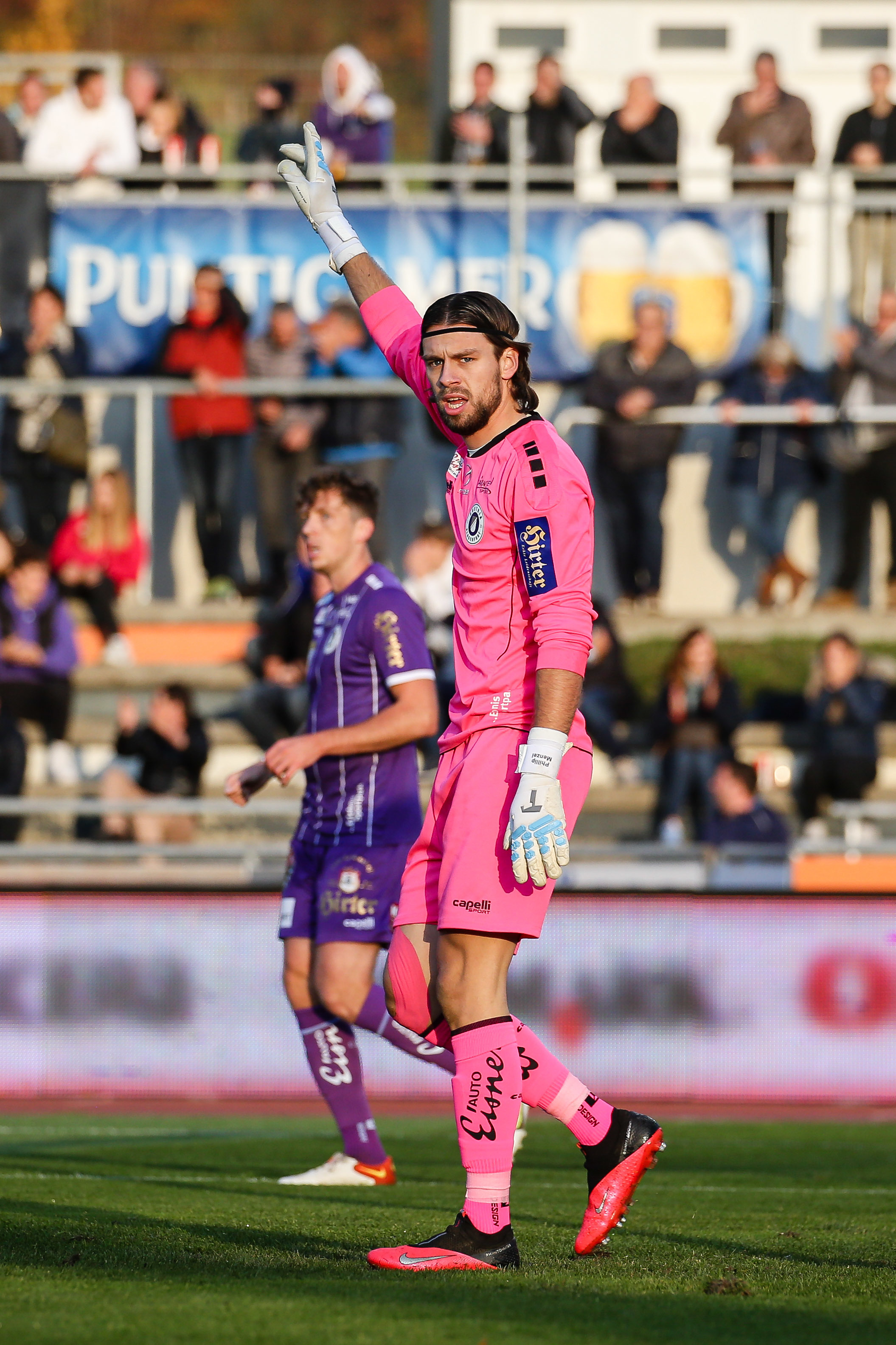 Der Torhüter des SK Austria Klagenfurt, Phillip Menzel, in einer rosaroten Torhütermontur auf dem Spielfeld vor der Zuschauertribüne