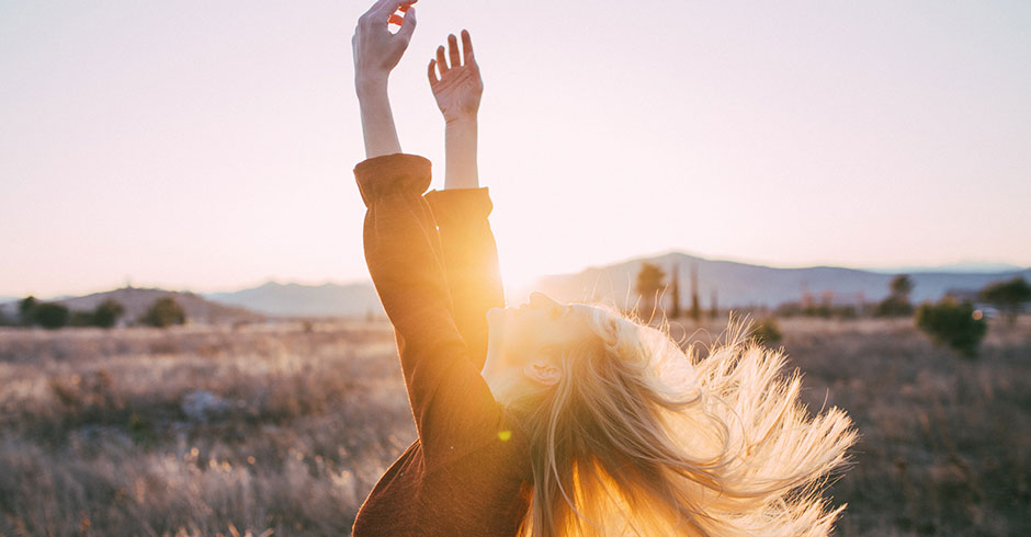 Frau streckt sich im Sonnenaufgang durch und ihre Arme dem Himmel entgegen | Credit: iStock.com/Primorac91